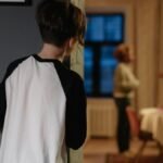 A child watches parents arguing from a doorway in a cozy home setting.