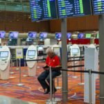 Busy airport terminal interior with flight information displays and check-in kiosks.