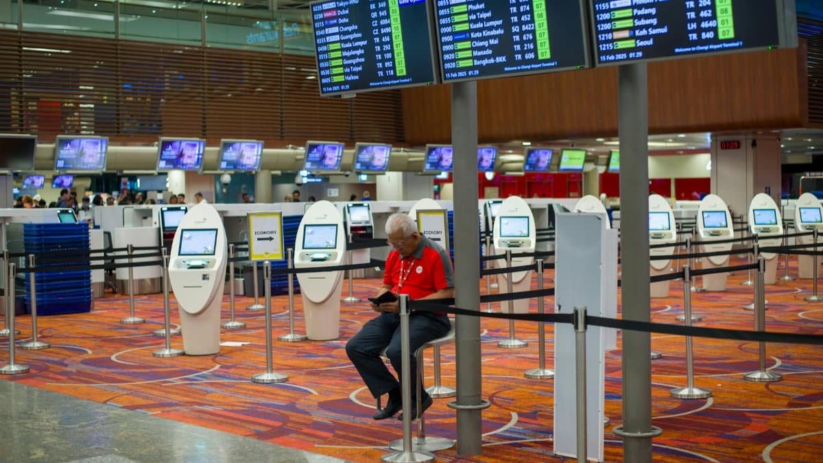 Busy airport terminal interior with flight information displays and check-in kiosks.