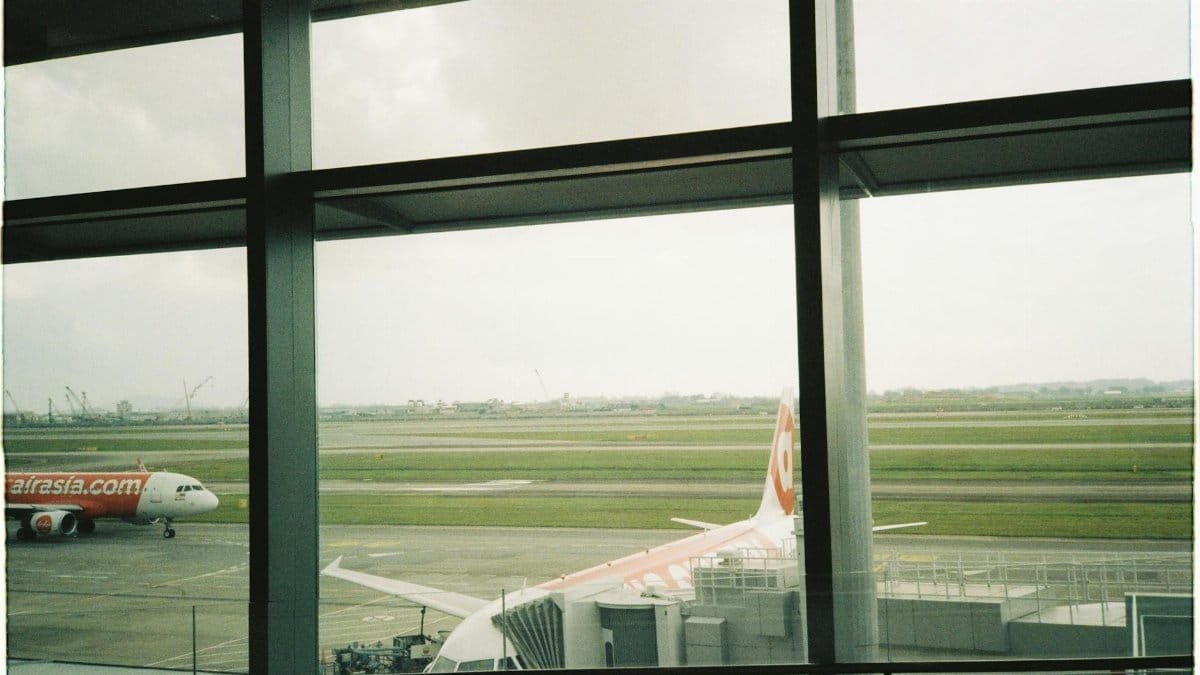 View of an AirAsia airplane parked at a terminal through large airport windows.