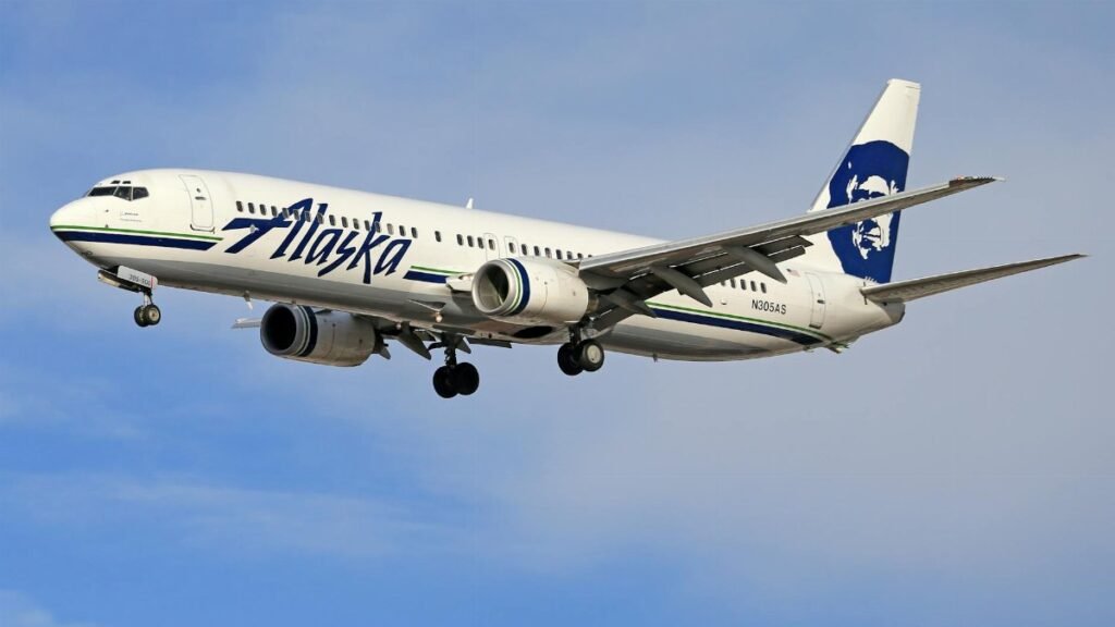Alaska Airlines Boeing jet soaring through a clear blue sky.