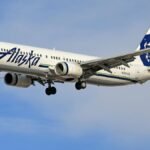 Alaska Airlines Boeing jet soaring through a clear blue sky.