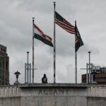 Three flags flying above a stone monument in downtown Albany, New York.