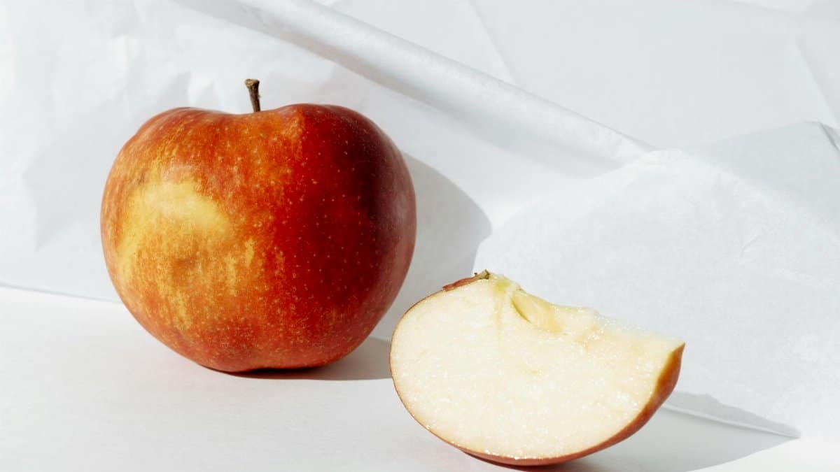 Close-up of a fresh red apple and a slice on a white surface, showcasing vibrant colors and texture.