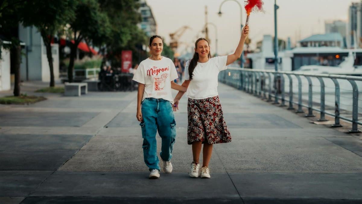 A joyful couple walks on the Buenos Aires waterfront, celebrating with a smoke flare.