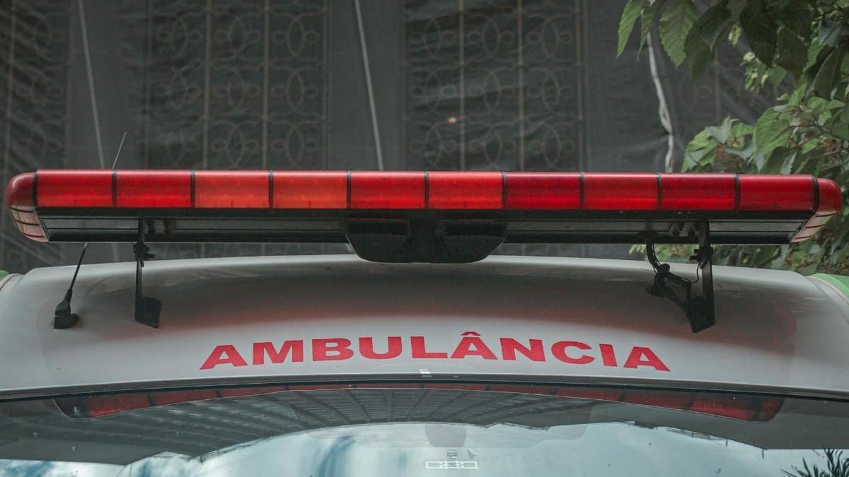 A close-up view of a city ambulance with a red siren light and Portuguese text 'AMBULÂNCIA'
