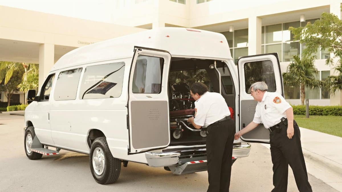 Two emergency responders load a stretcher into an ambulance outside a medical facility.