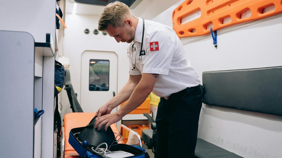 A paramedic organizing medical equipment in an ambulance interior.