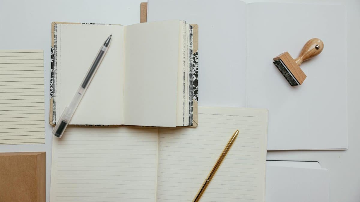 Flat lay of stationery items including notepads, pens, and a stamp on a white background.