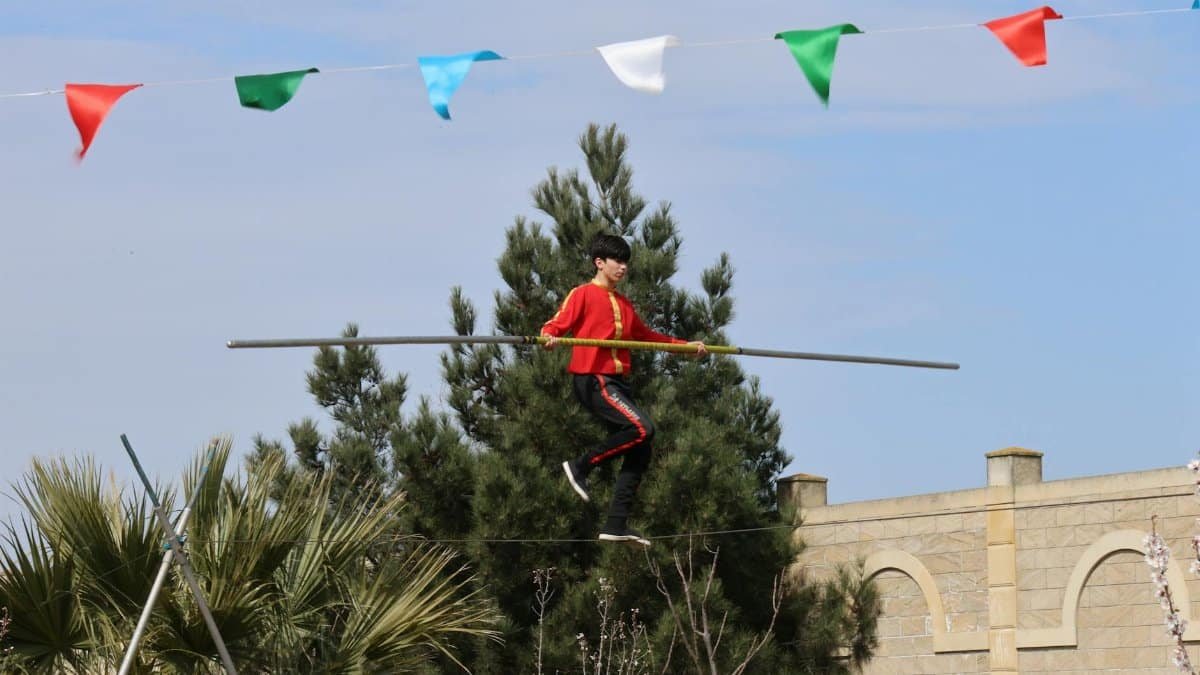 A skilled performer balances on a tightrope outdoors beneath colorful flags.