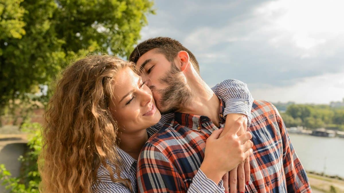 Happy couple sharing a loving embrace outdoors with a scenic background.
