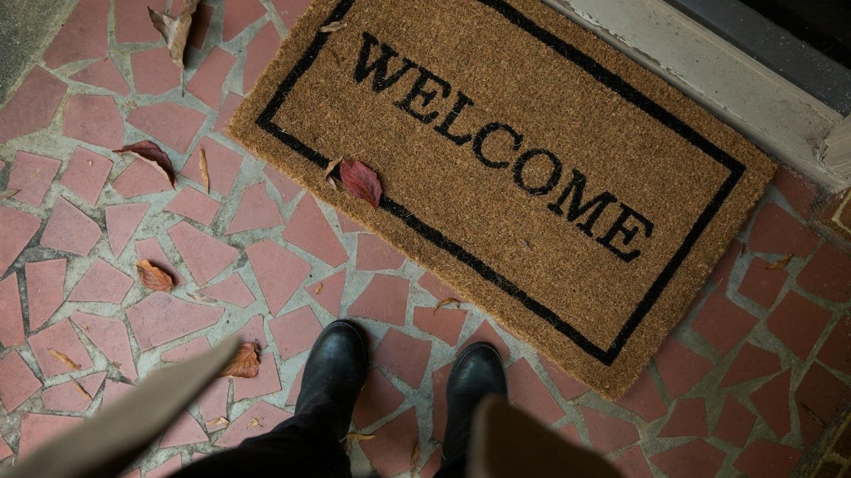 Welcome mat on a tiled porch with boots visible. Perfect for home decor or hospitality themes.