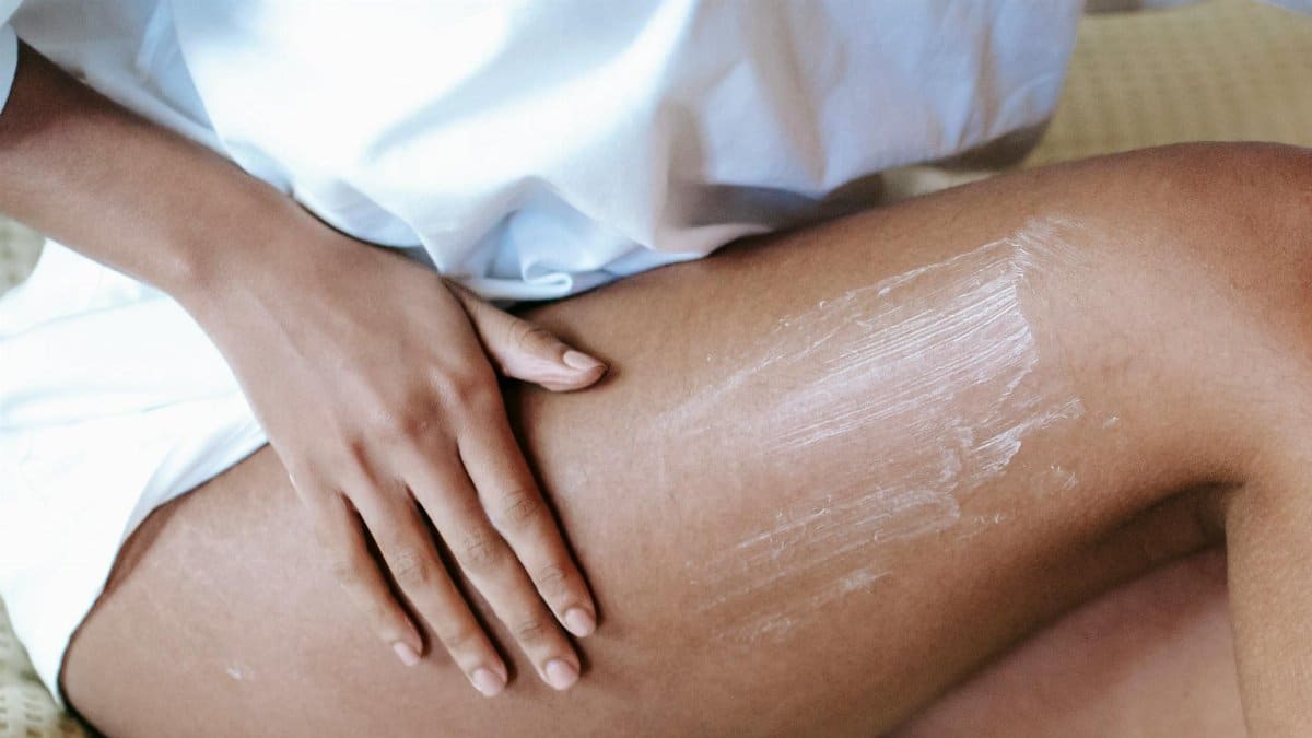 A woman gently applying moisturizing cream to her leg for skin care routine.