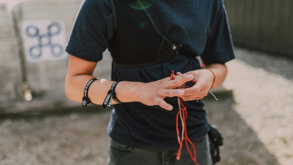 A young archer adjusts wristbands and equipment outdoors, preparing for archery practice on a sunny day.