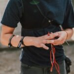 A young archer adjusts wristbands and equipment outdoors, preparing for archery practice on a sunny day.