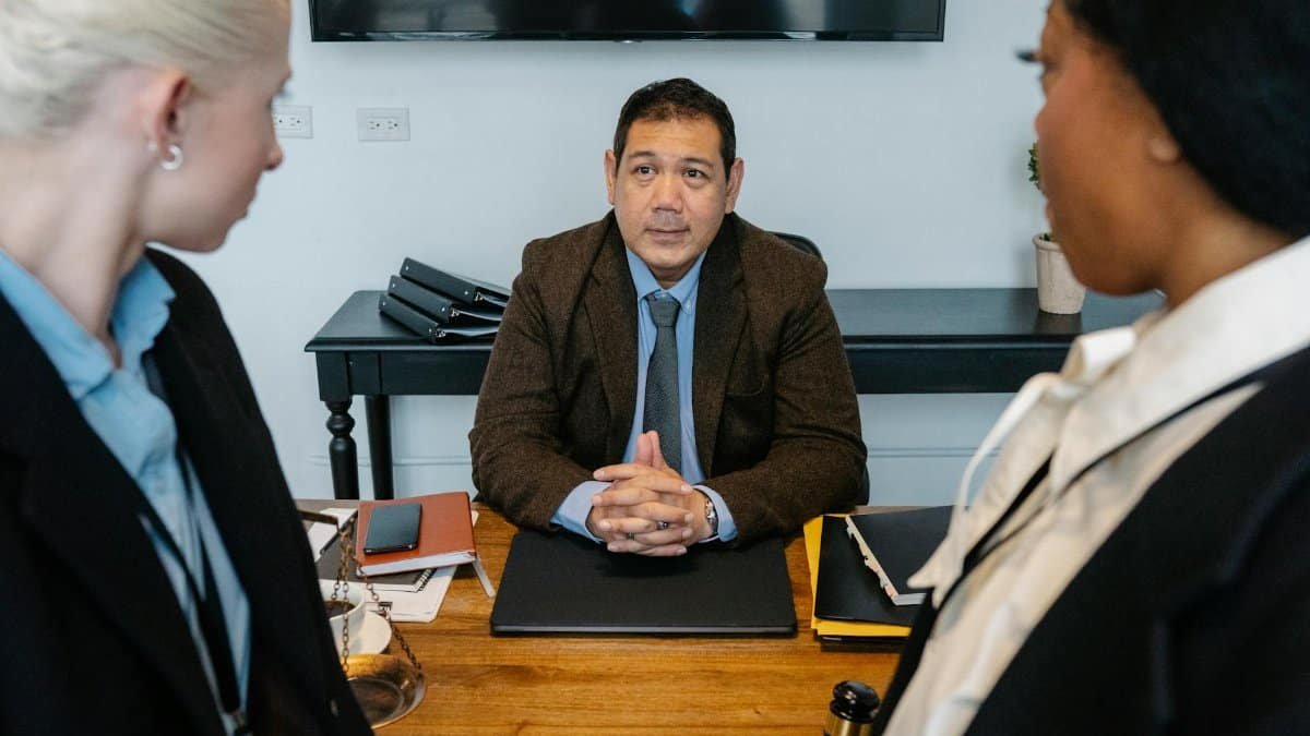 Three diverse attorneys in a formal meeting at a law firm office table.