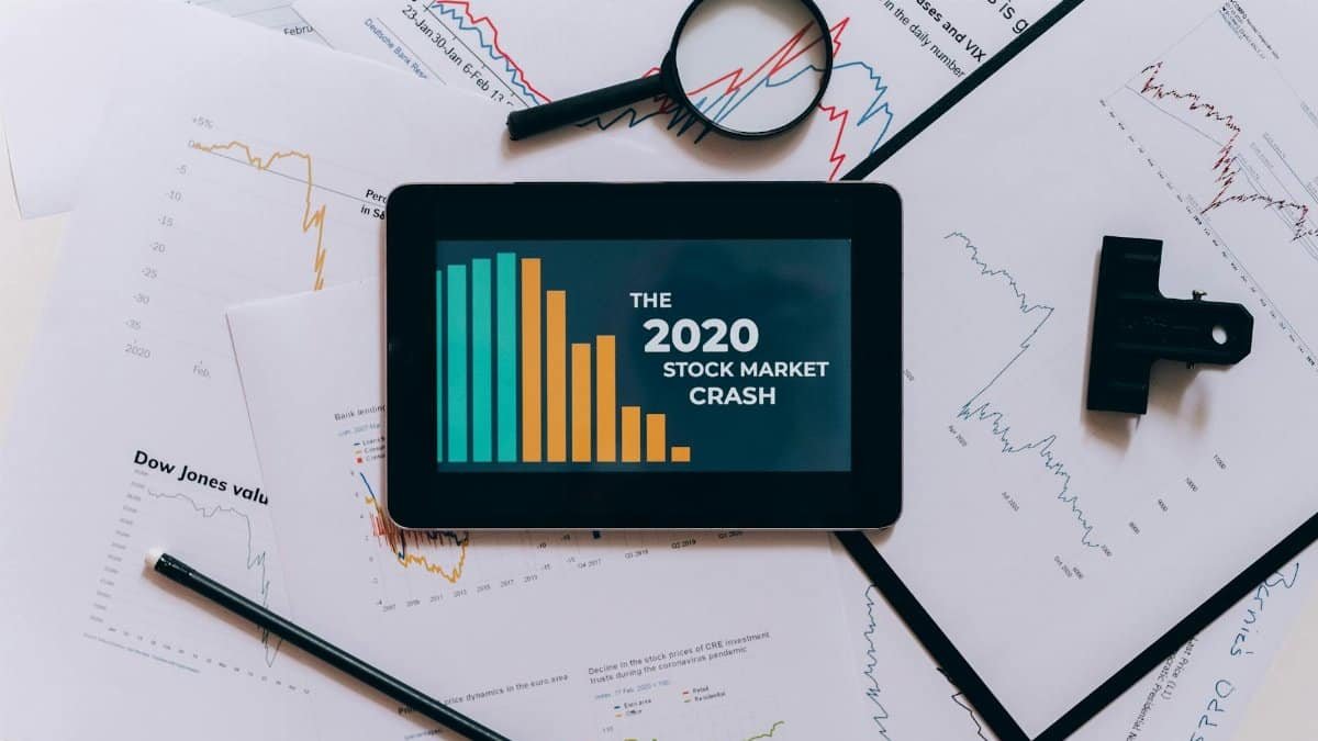 Flat lay of tablet showing 2020 stock market crash with charts and papers.