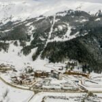 Drone shot of a snowy mountain ski resort with coniferous trees and snowy peaks.