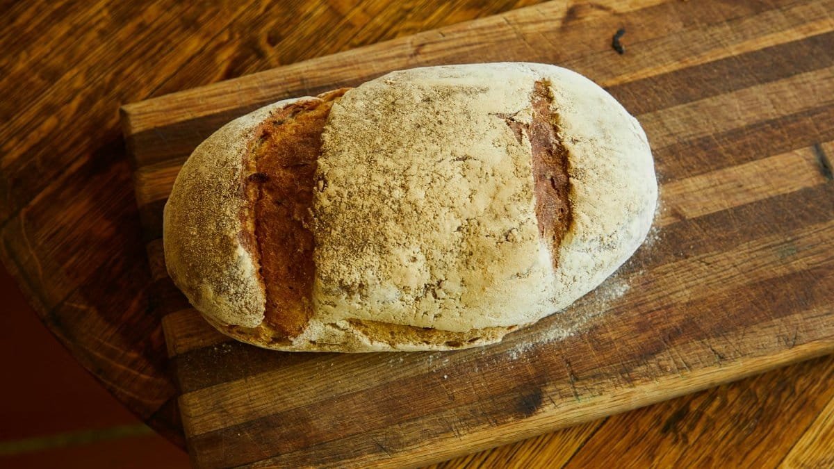 A freshly baked rustic loaf of bread on a wooden cutting board, ideal for culinary content.