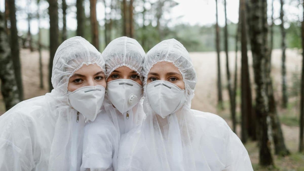 Three women in protective suits and masks in a forest, highlighting environmental protection.