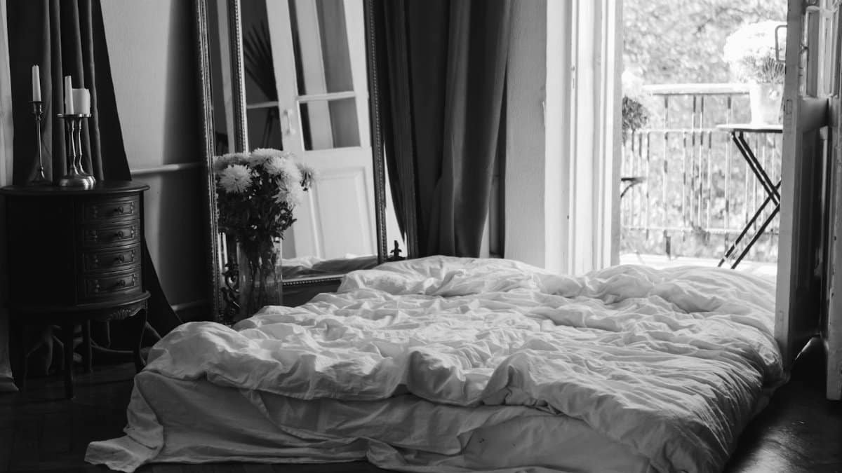 Black and white image of a stylish bedroom with a balcony view, cozy bed, and elegant decor.