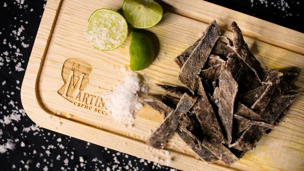 Top view of dried meat strips with lime and sea salt on a rustic wooden board.