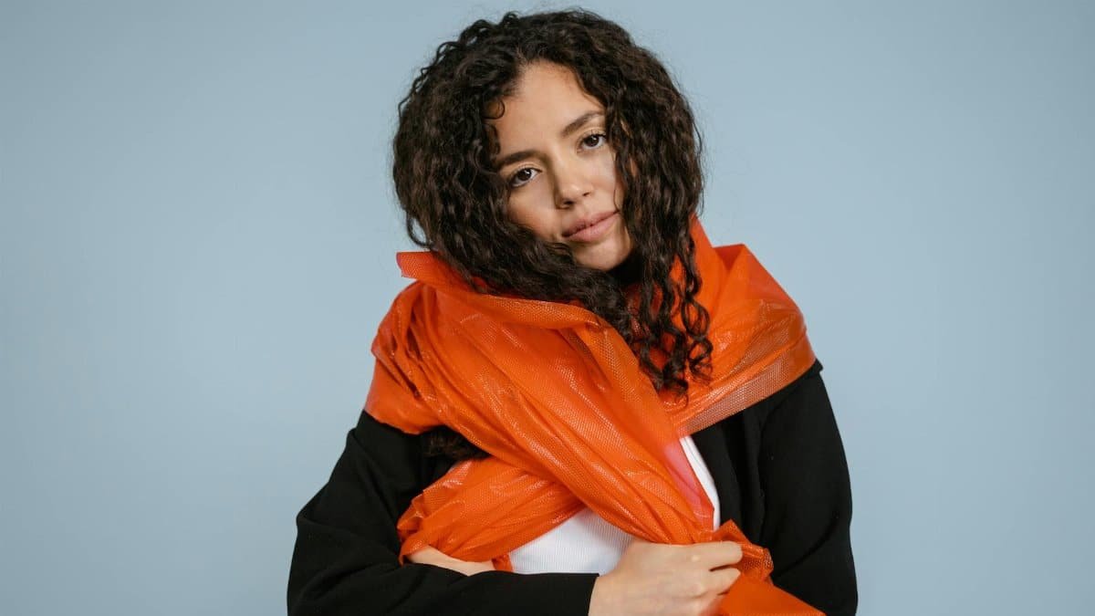 Portrait of a woman wrapped in orange plastic, highlighting environmental themes.