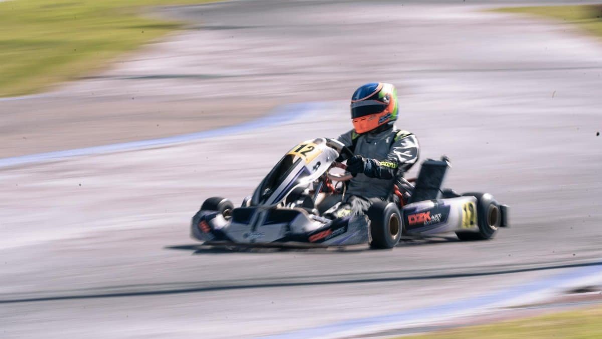 Dynamic action shot of a racer speeding in a go-kart on an outdoor track.