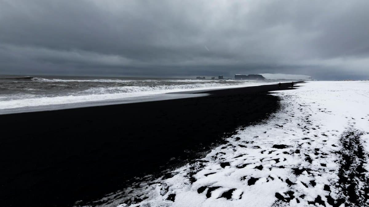 Stunning black sand beach with snow contrast under ominous clouds, captured in winter.