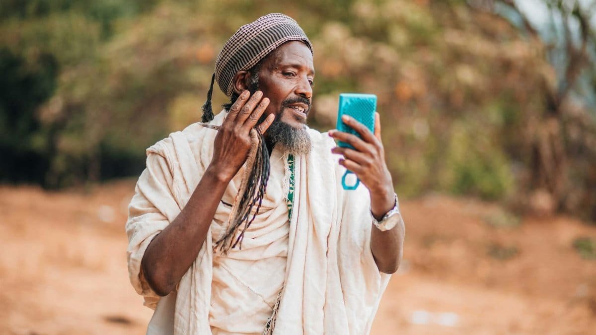 African man in traditional attire uses a smartphone outdoors. Concept of technology blending with culture.