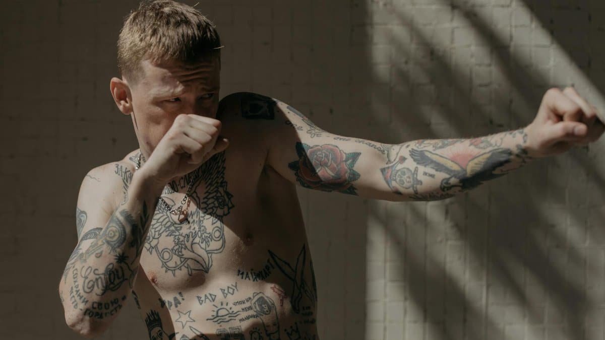 Tattooed boxer demonstrating a fighting stance with dramatic lighting indoors.