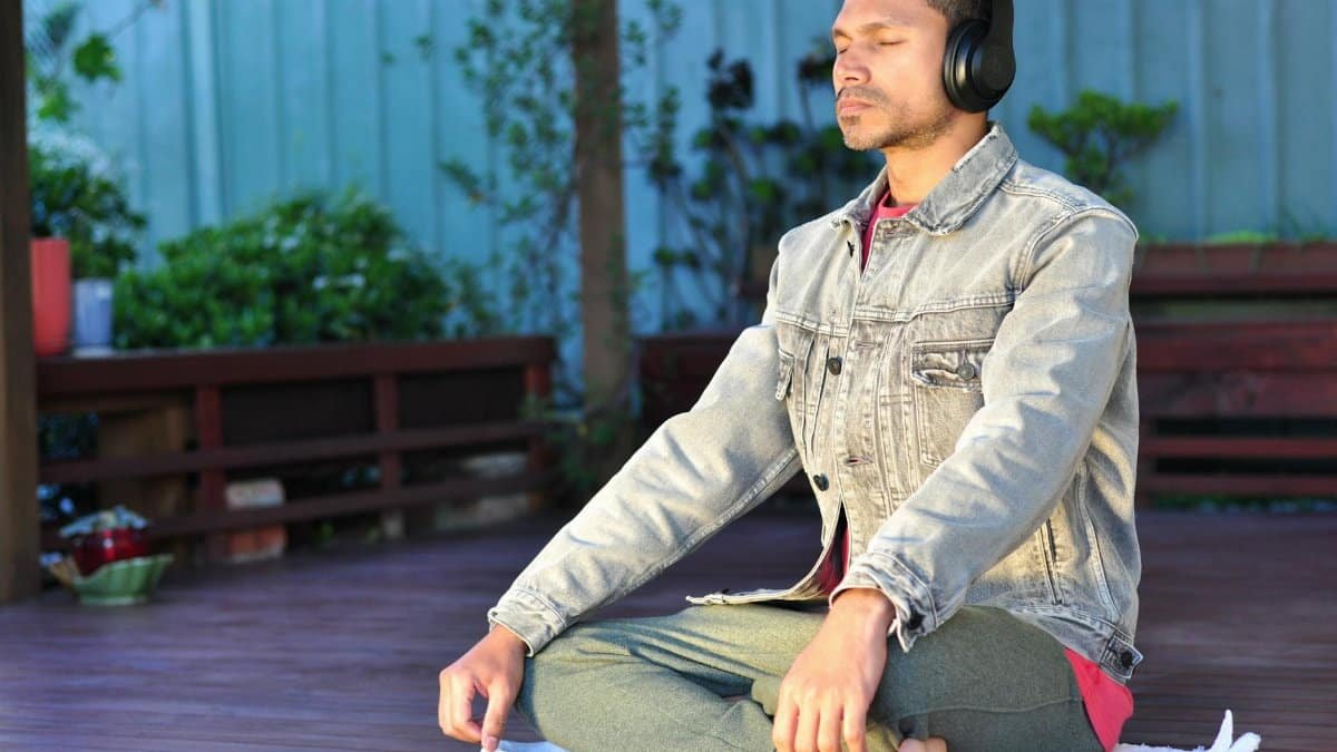 Adult man practicing meditation and relaxation with headphones in a serene outdoor setting.