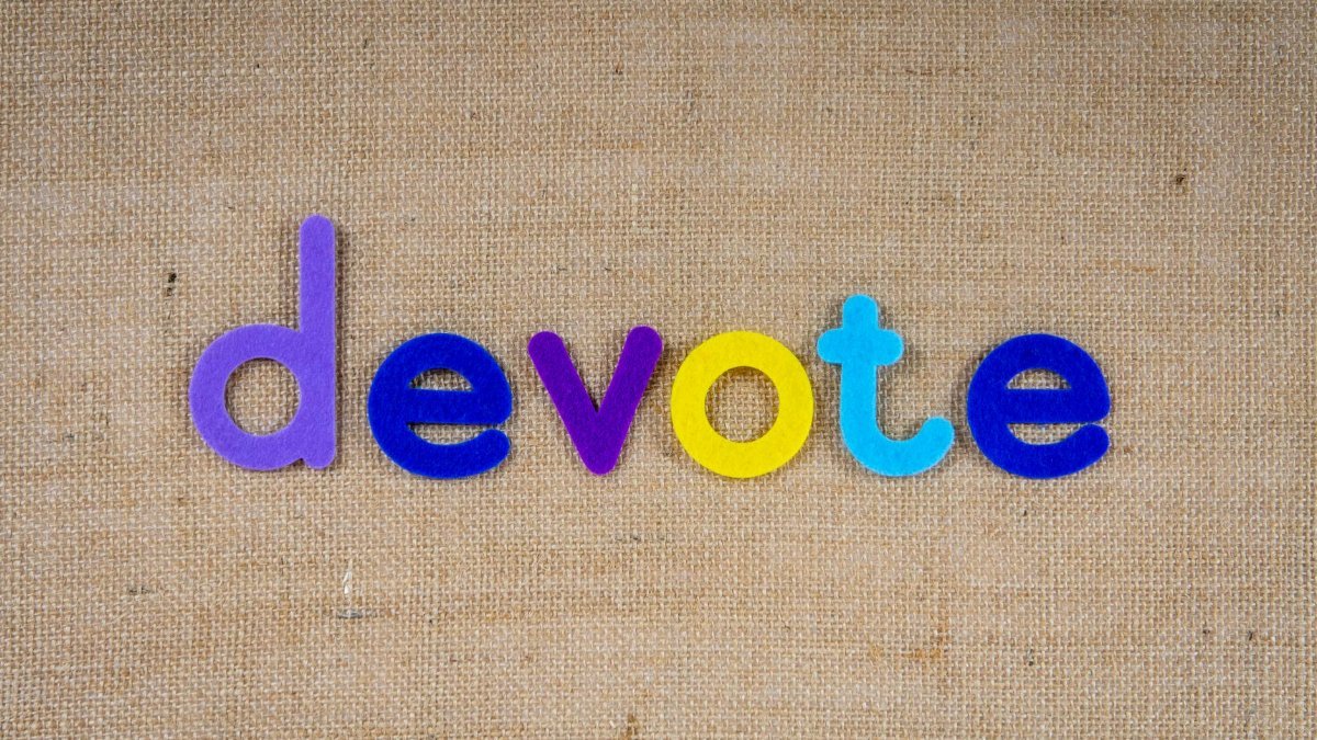 Colorful letters forming the word 'devote' on burlap fabric background.