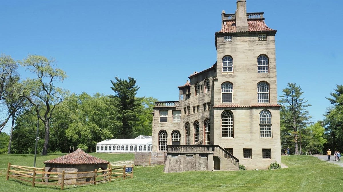 Explore the iconic Fonthill Castle surrounded by lush greenery under a clear blue sky in Doylestown, PA.