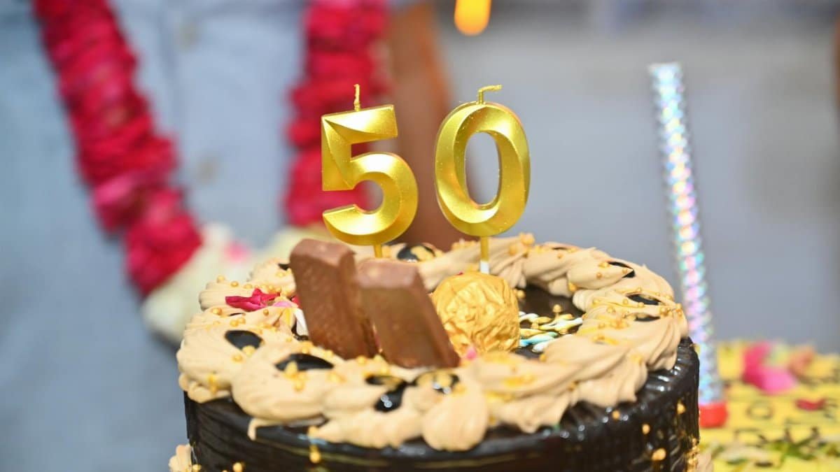 Elegant chocolate cake with golden 50th anniversary candles and decorations.
