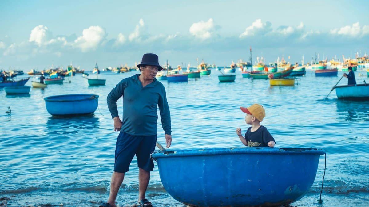 A man and child by the seaside, surrounded by colorful fishing boats.