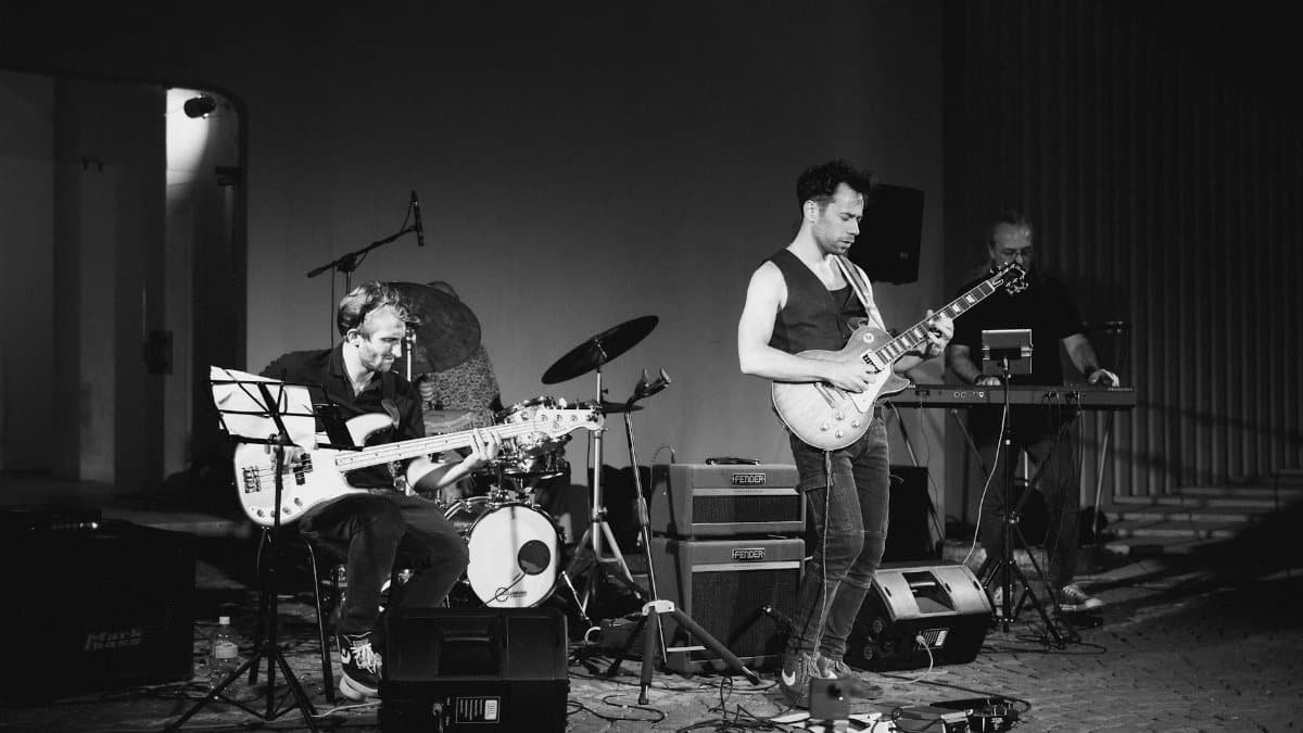 A dynamic black and white photo of a live jazz band performing with guitar, bass, and piano on stage.