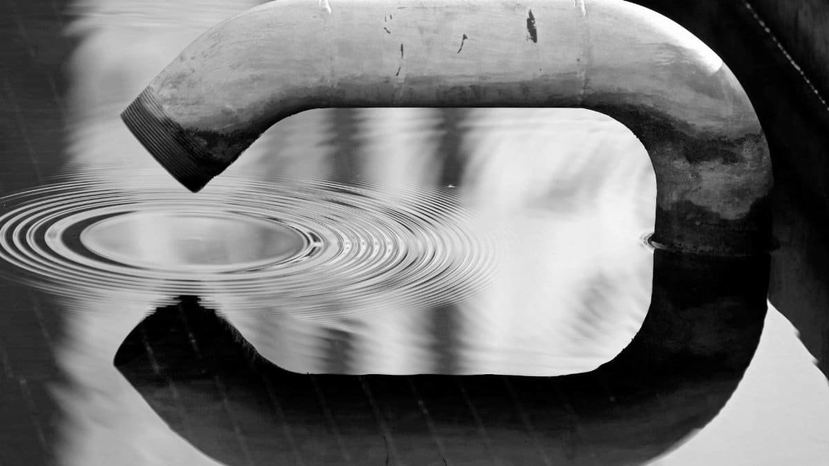 Black and white image of a pipe creating ripples in water. An abstract reflection scene.