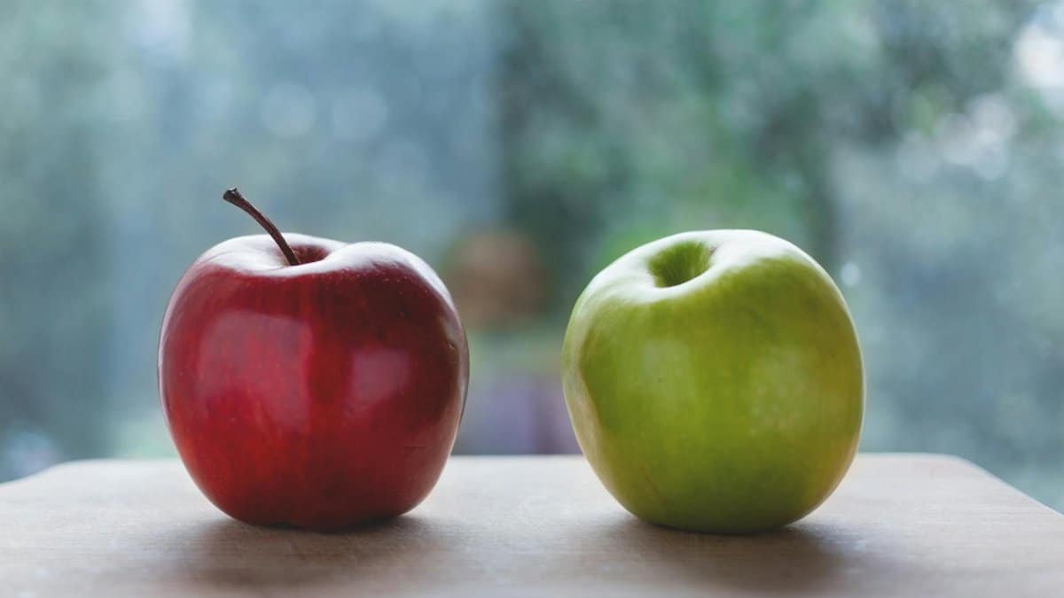 Two fresh apples, one red and one green, sitting on a wooden surface indoors.