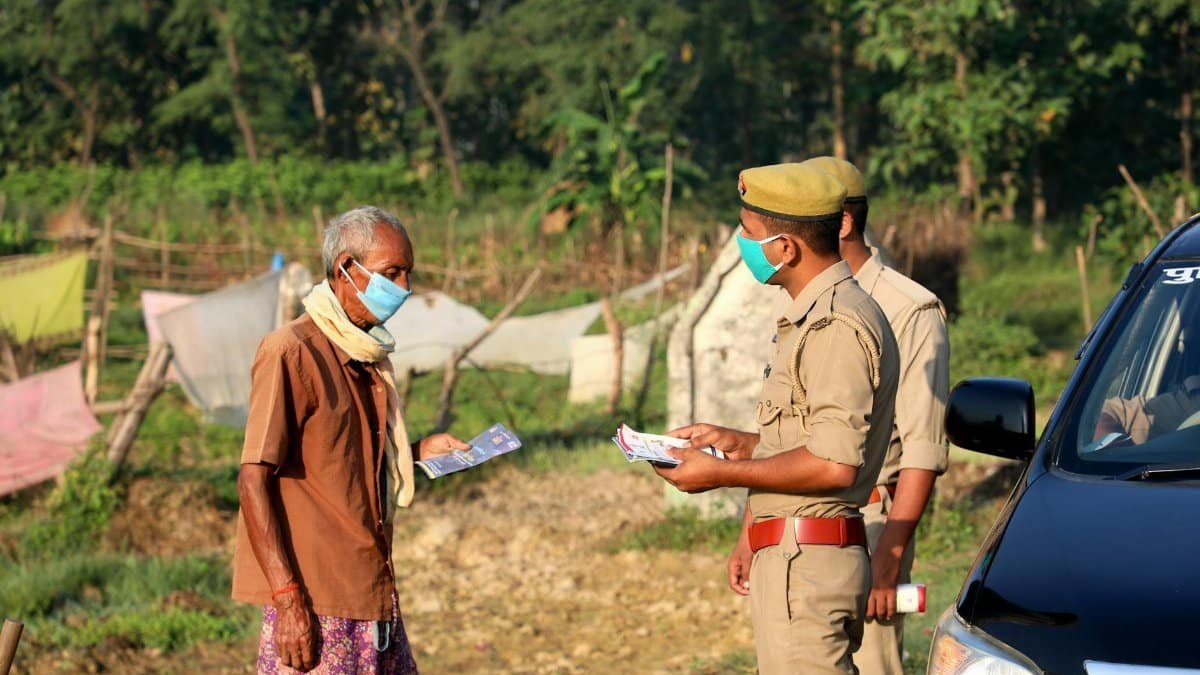 Police officers distribute flyers to a masked villager outdoors, emphasizing safety during the pandemic.