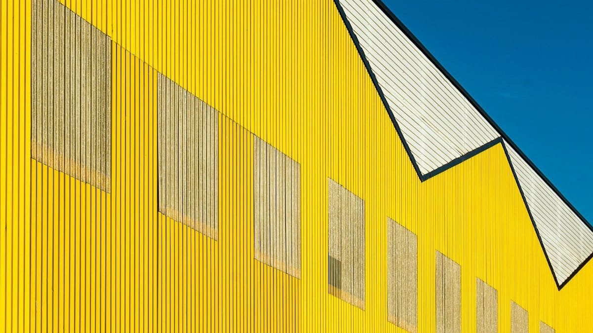 Close-up shot of a geometric yellow industrial building with clear blue sky.