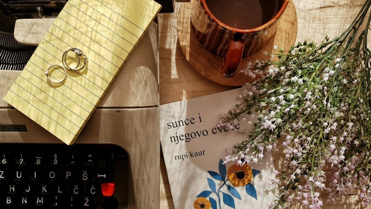 Charming vintage flatlay with a typewriter, coffee mug, flowers, and rings on a wooden surface.