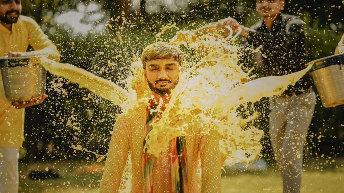 Indian man involved in a traditional pre-wedding ritual with vibrant water splashing.