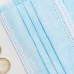 Flatlay of surgical face masks and euro coins, symbolizing pandemic economic challenges.
