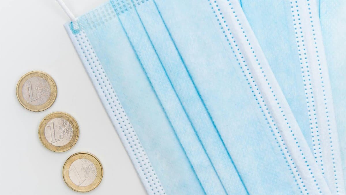 Flatlay of surgical face masks and euro coins, symbolizing pandemic economic challenges.