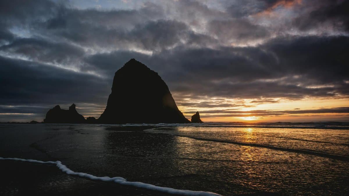 Dramatic sunset highlighting Haystack Rock and reflections on Cannon Beach, Oregon.