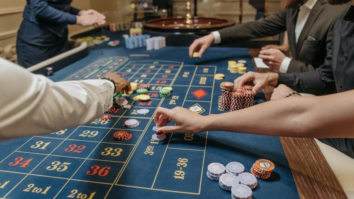 A lively casino scene with players placing bets and handling gaming chips on a roulette table.