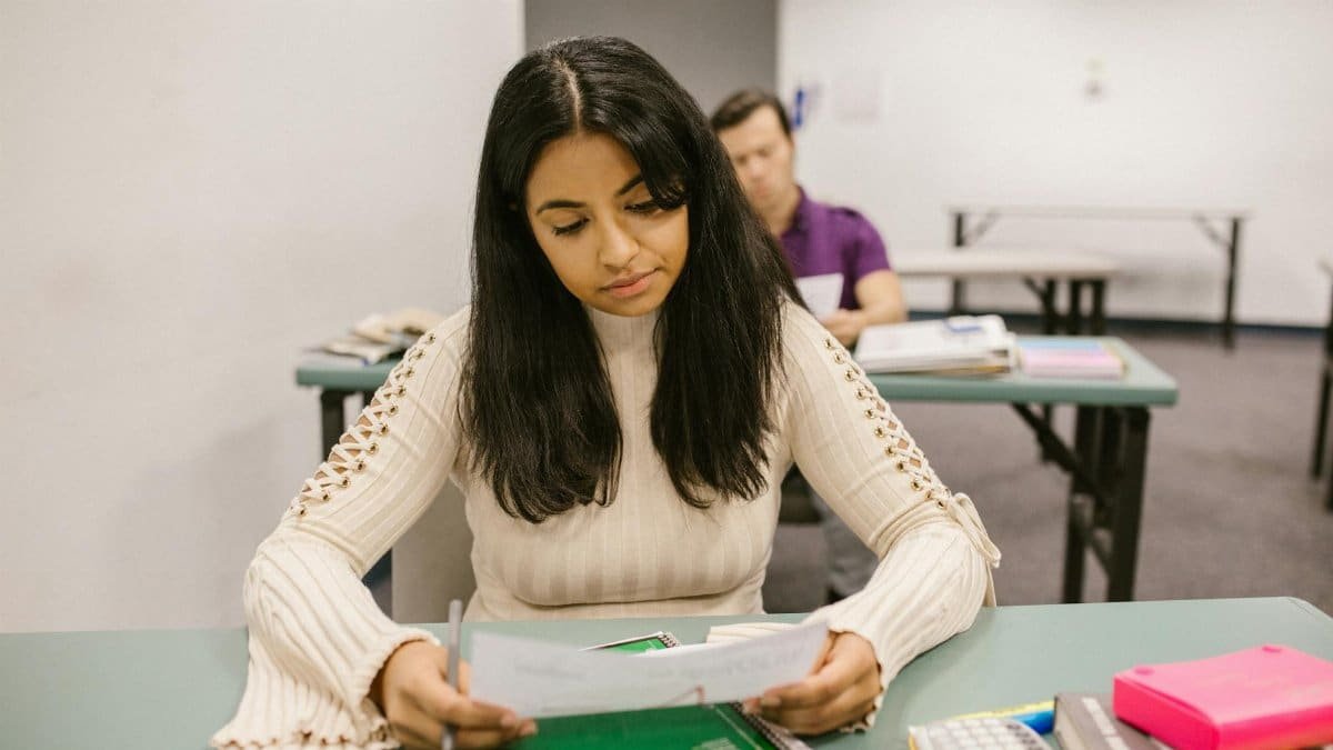 Female college student looking at exam results in a classroom setting, focused and thoughtful.