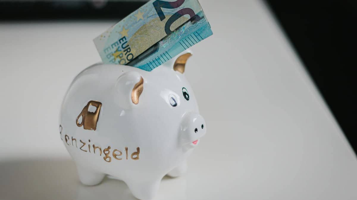 A white piggy bank with a €20 note inserted, symbolizing savings.