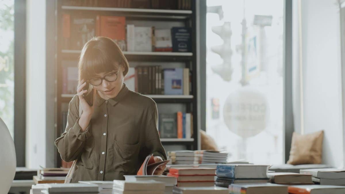 A woman reading a book and talking on the phone in a cozy bookstore setting.